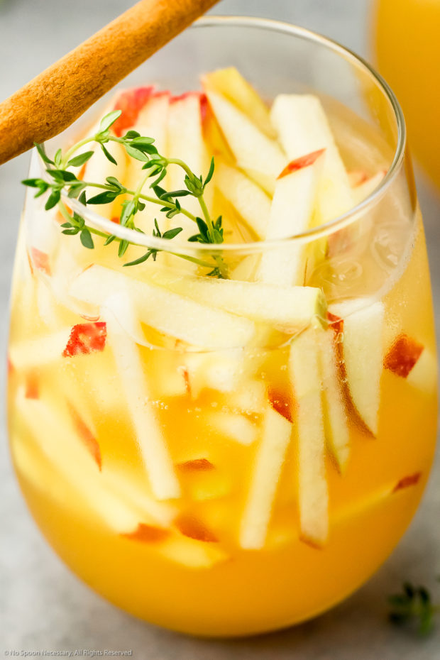 Angled photo of a cocktail glass filled with an Apple Cider Cocktail, garnished with matchstick cut apples, fresh thyme sprigs and a cinnamon stick.