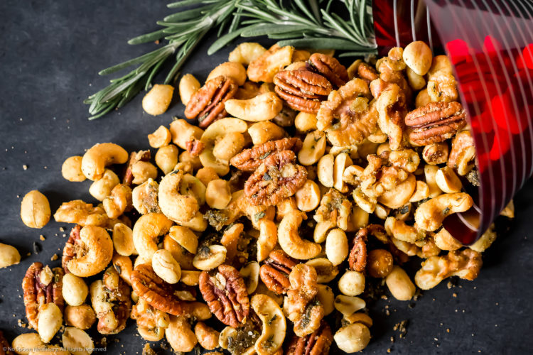 Overhead, landscape photo of Savory & Spicy Rosemary Roasted Nuts spilling out of a red martini glass with fresh rosemary.