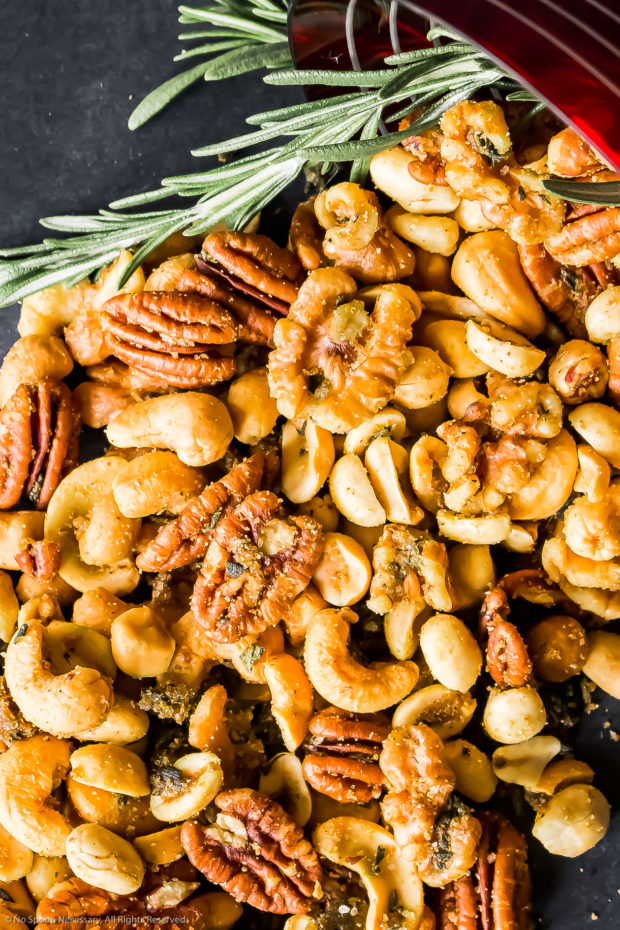 Overhead photo of a pile of homemade spiced nuts (pecans, cashews and peanuts) on a black surface.