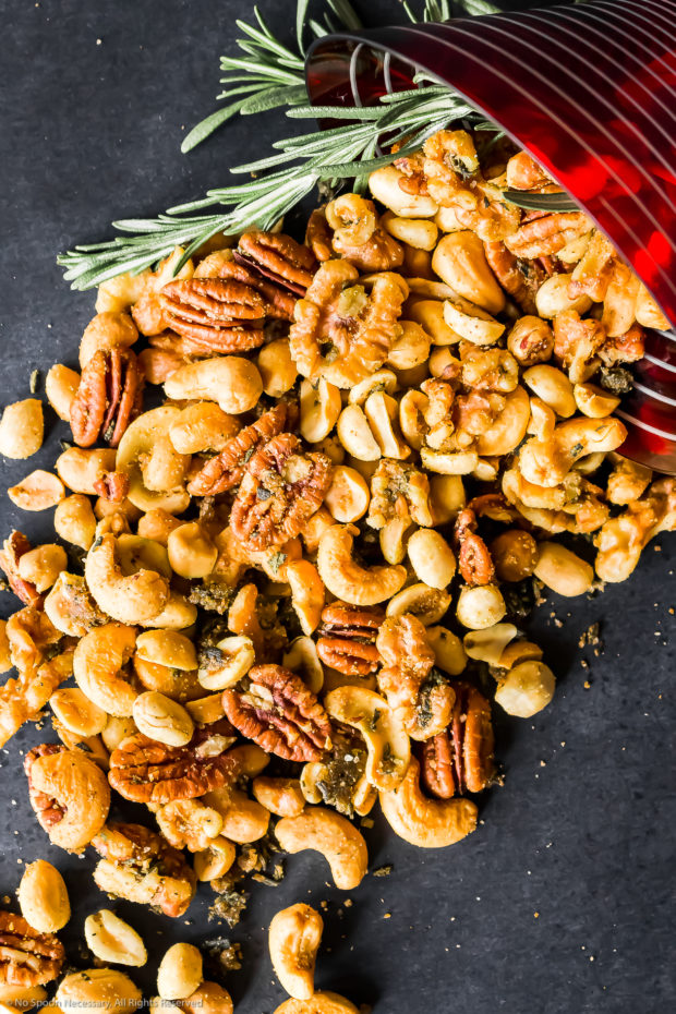 Overhead photo of homemade Roasted Nuts spilling out of a tipped over red martini glass with fresh rosemary.