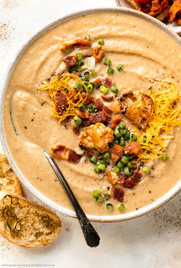 Overhead photo of a bowl of healthy roasted cauliflower soup with a spoon inserted into the soup.