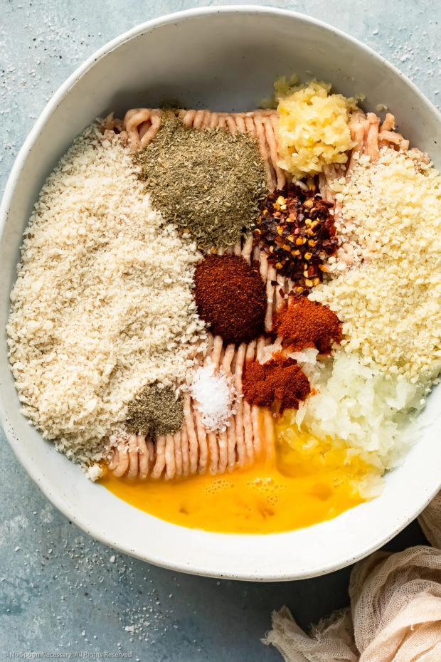Overhead photo of all the ingredients needed to prepare spicy chicken meatballs neatly organized by individual ingredient in a large white mixing bowl.