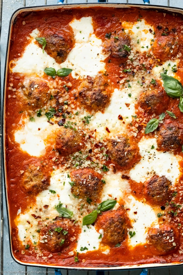 Overhead, up-close photo of spicy chicken meatballs baked in vodka tomato sauce, topped with cheese and garnished with fresh herbs and grated parmesan.