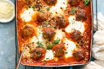 Overhead photo of a large baking dish filled with baked spicy chicken meatballs topped with cheese and basil with a large serving spoon inserted into the dish.