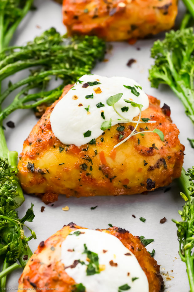 Angled, up-close photo of baked diavolo chicken thigh topped with a dollop of burrata cheese and surrounded by cooked broccoli.