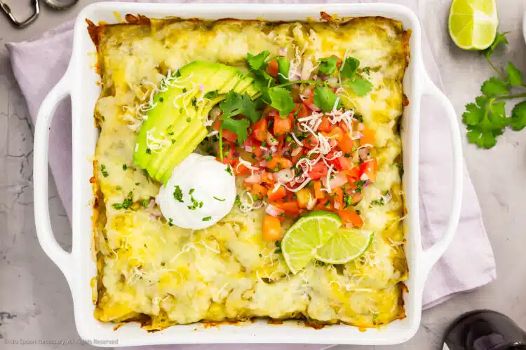 Overhead photo of enchilada casserole with chicken in square white baking dish.