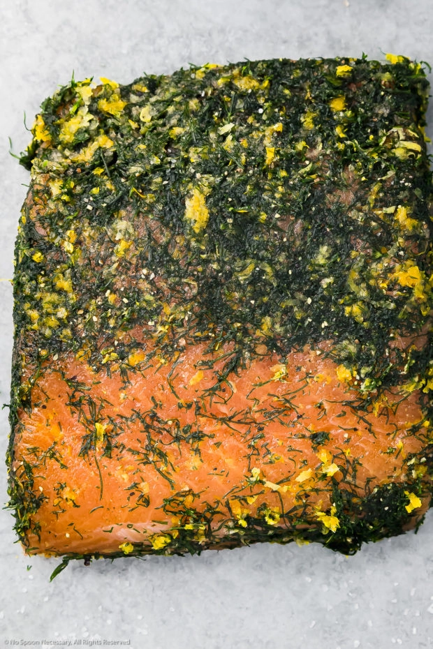Overhead photo of a filet of salmon that has been salt-cured and wrapped with fresh dill, with part of the dry brine scrapped off the top exposing the cured salmon.