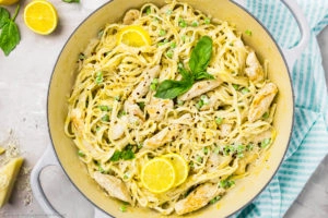 Overhead photo of creamy lemon chicken pasta with fresh basil and peas in a large gray skillet.