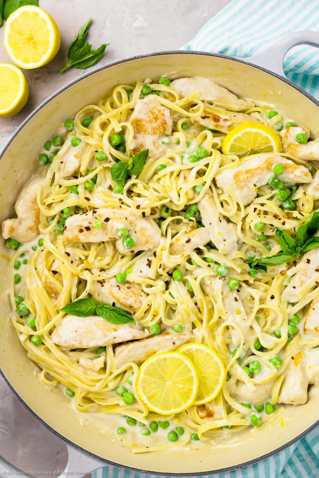 Overhead photo of creamy lemon chicken pasta with basil and peas in a large gray skillet.