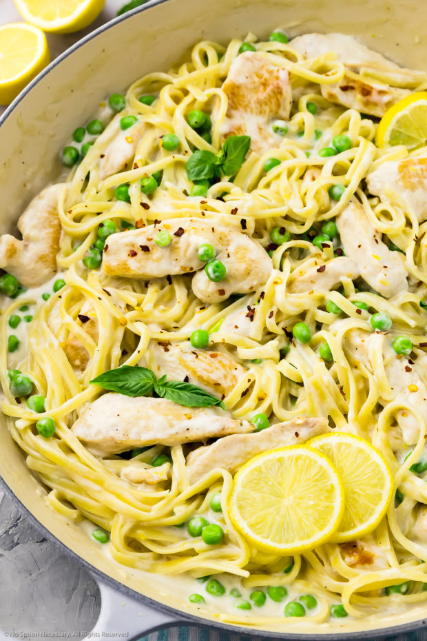 Angled, close-up photo of creamy pasta with chicken, peas, fresh basil and slices of lemon in a large skillet.