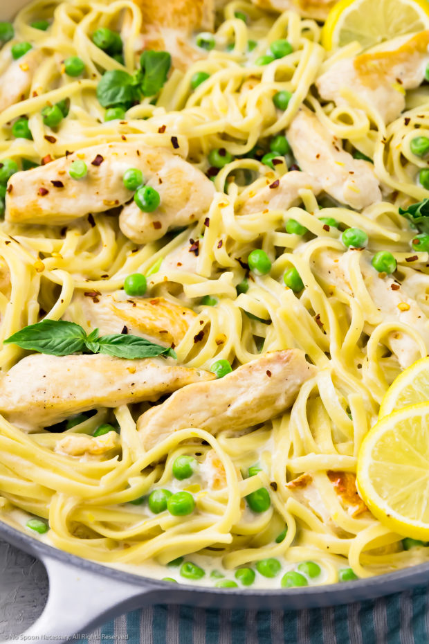 Angled, close-up photo of creamy linguine pasta with chicken, lemon slices, peas and basil.