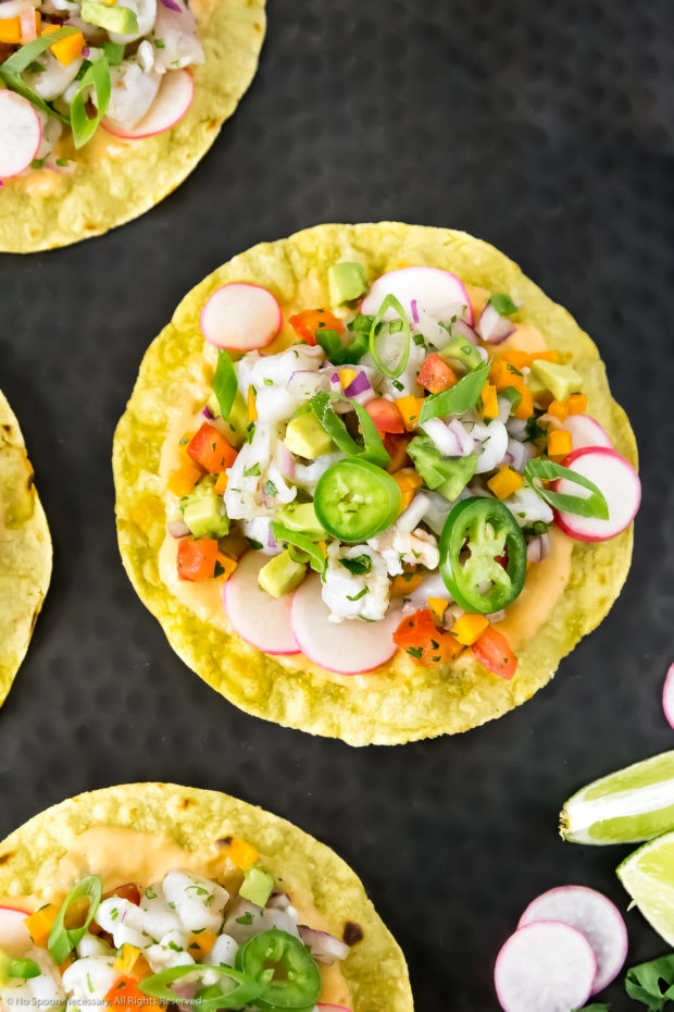 Overhead photo of Mexican Shrimp Ceviche Tostadas on a black platter with lime wedges, and sliced radishes.