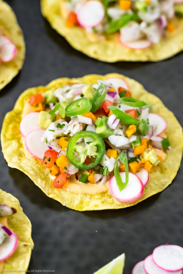 Angled photo of Shrimp Ceviche Tostadas on a black platter with lime wedges, and sliced radishes.