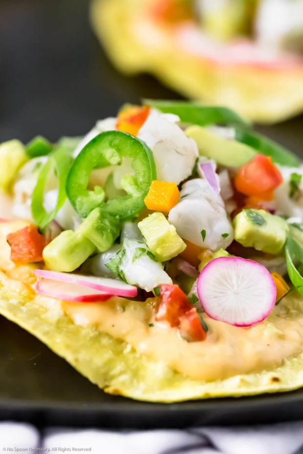 Straight on, close-up photo of a Mexican Ceviche Tostada on a black platter with more tostadas blurred in the background.