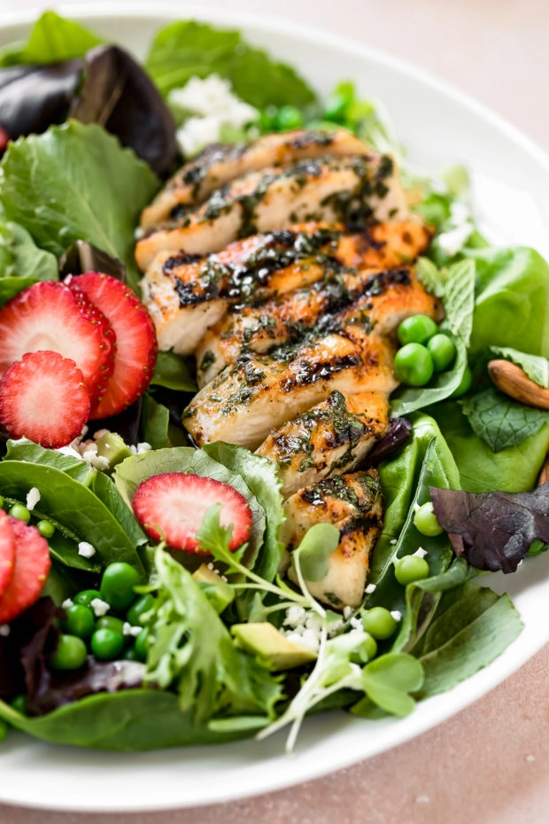 Angled shot of a Strawberry Salad with spinach, grilled chicken, fresh peas and avocado on white salad plate.