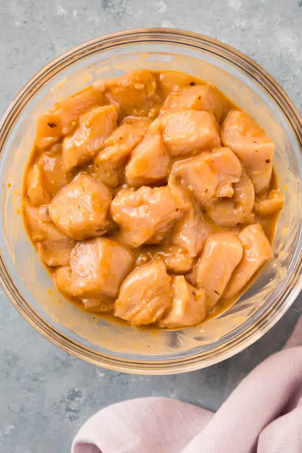 Overhead photo of raw chicken pieces marinating in peanut sauce.