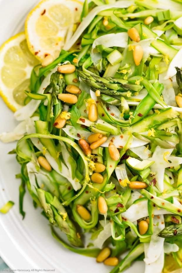 Overhead, up close shot of raw asparagus salad tossed with and fennel pine nuts and thin lemon slices. 