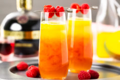 Straight on photo of two champagne cocktails made with fresh fruit puree and blood orange liqueur in a tall champagne flutes.