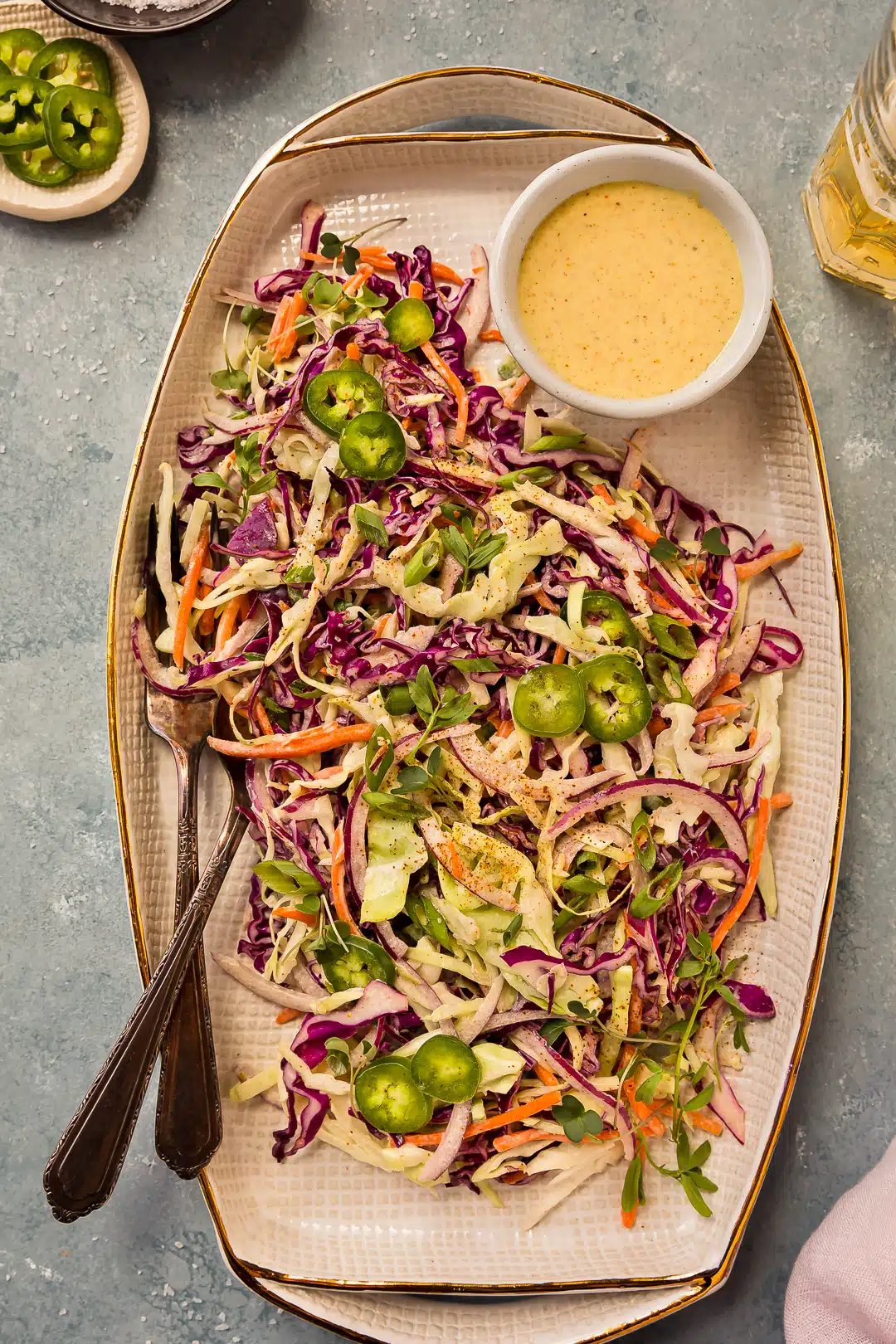 Overhead photo of coleslaw with jalapenos, cabbage, and cilantro on a white serving platter with a ramekin of dressing on the side.