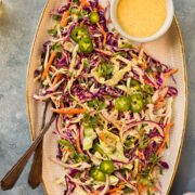 Overhead, landscape photo of jalapeno coleslaw on a white and gold trim platter with a fork and spoon tucked into the slaw.