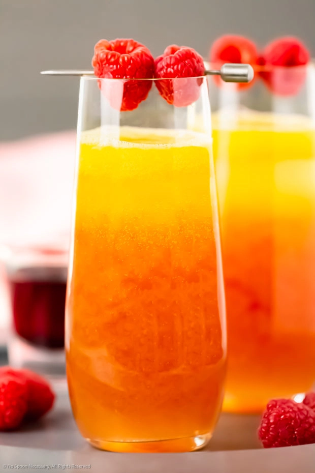 Straight on photo of a layered mimosa made with yellow mango puree and red chambord liqueur in a tall champagne flute.