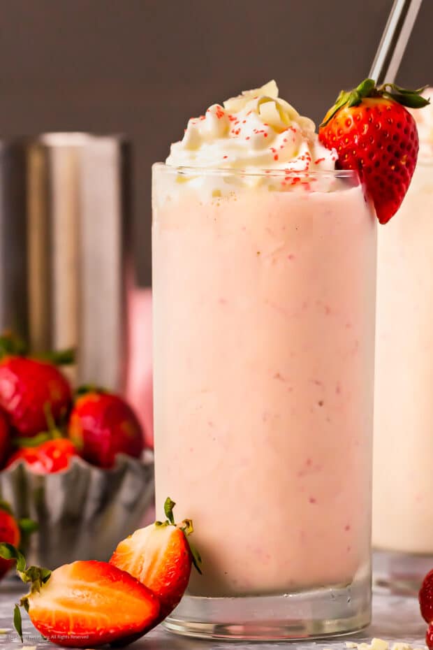 Photo of a spiked strawberry milkshake topped with whipped cream, red sprinkles, and shaved white chocolate.