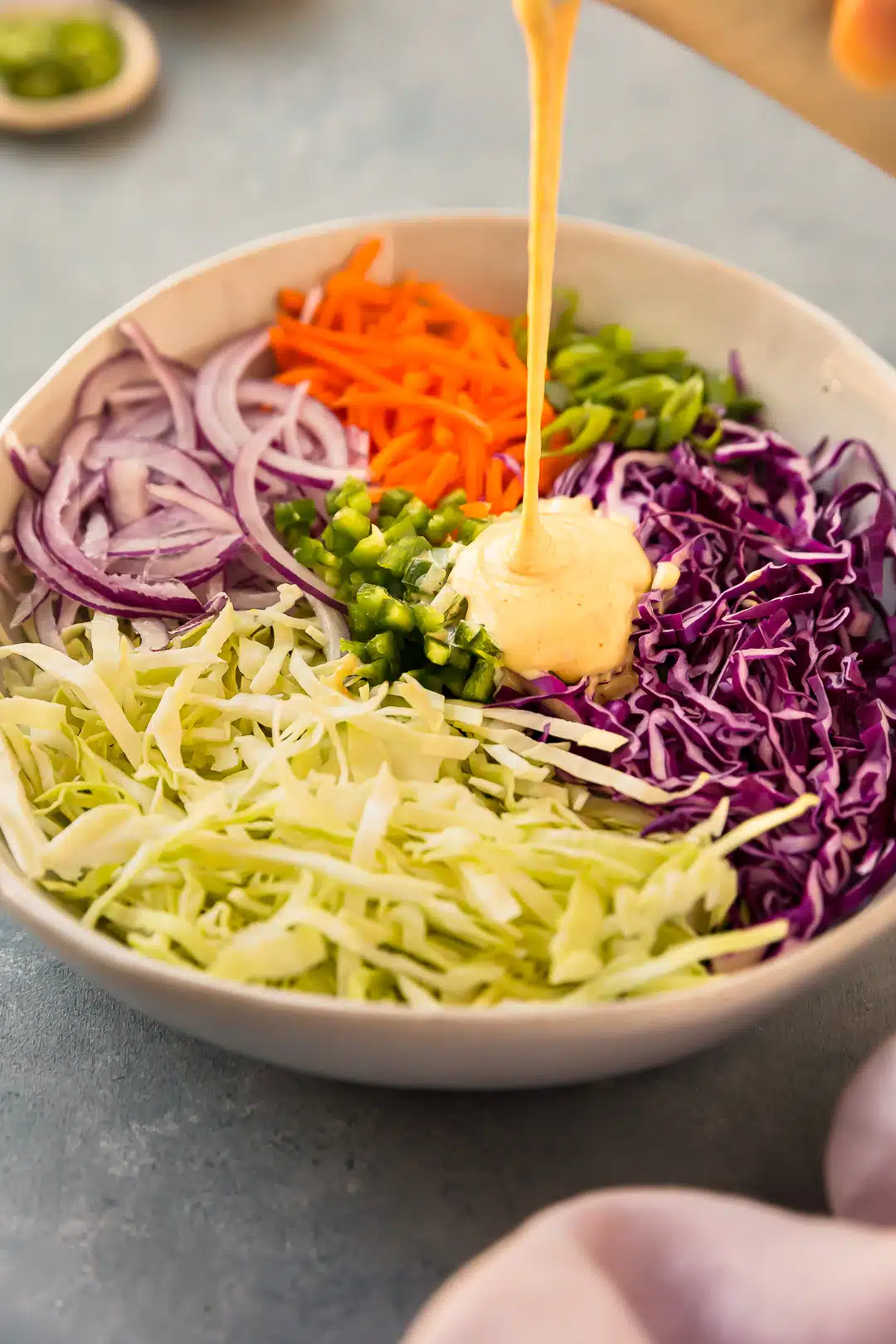 Angled, action photo of dressing being poured over cabbage jalapeno slaw in a large mixing bowl.