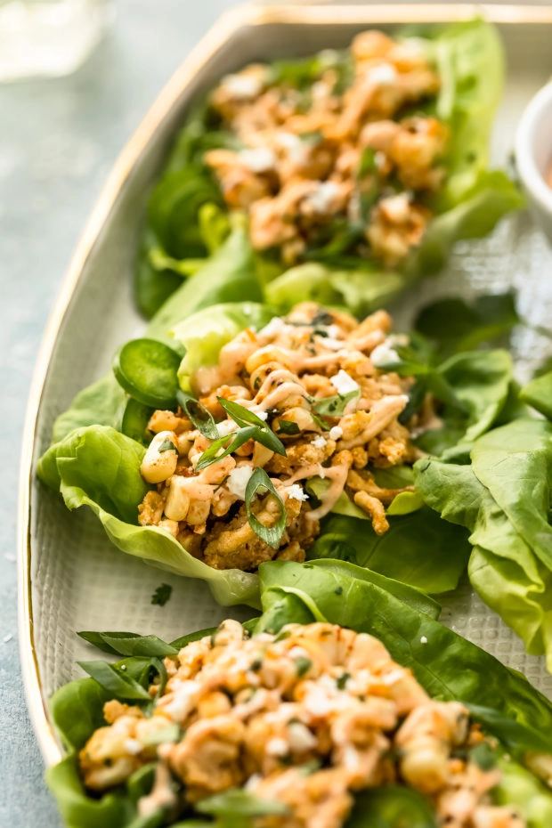 Angled shot of Mexican Lettuce Wraps on a white platter with a wine glass barely visible and blurred in the background.