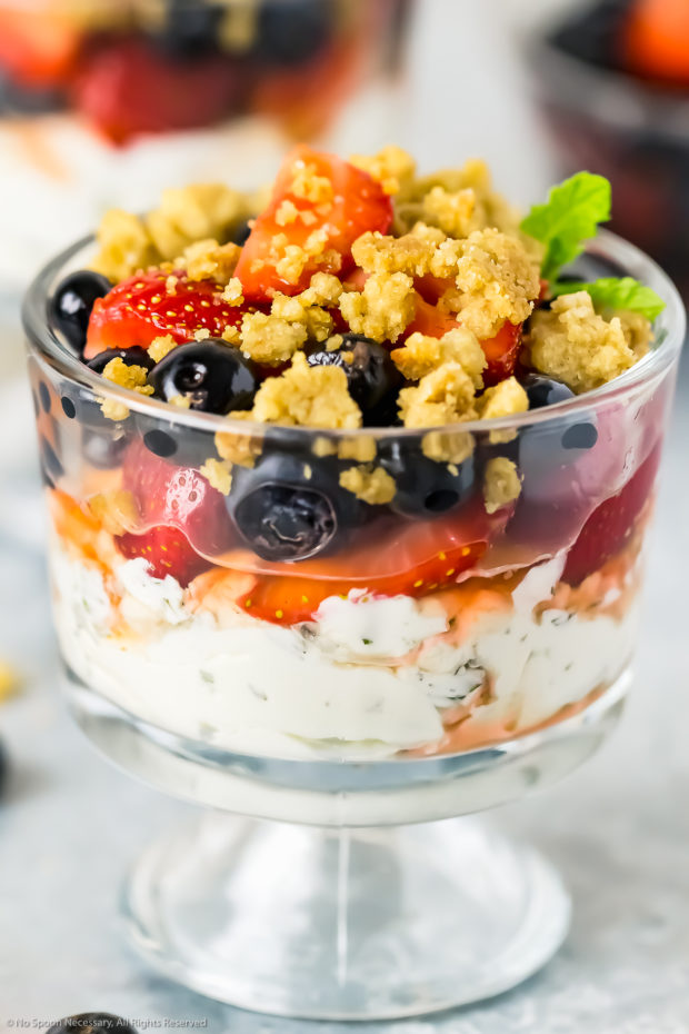 Angled photo of a fresh fruit parfait in a small parfait glass with additional parfaits blurred in the background.