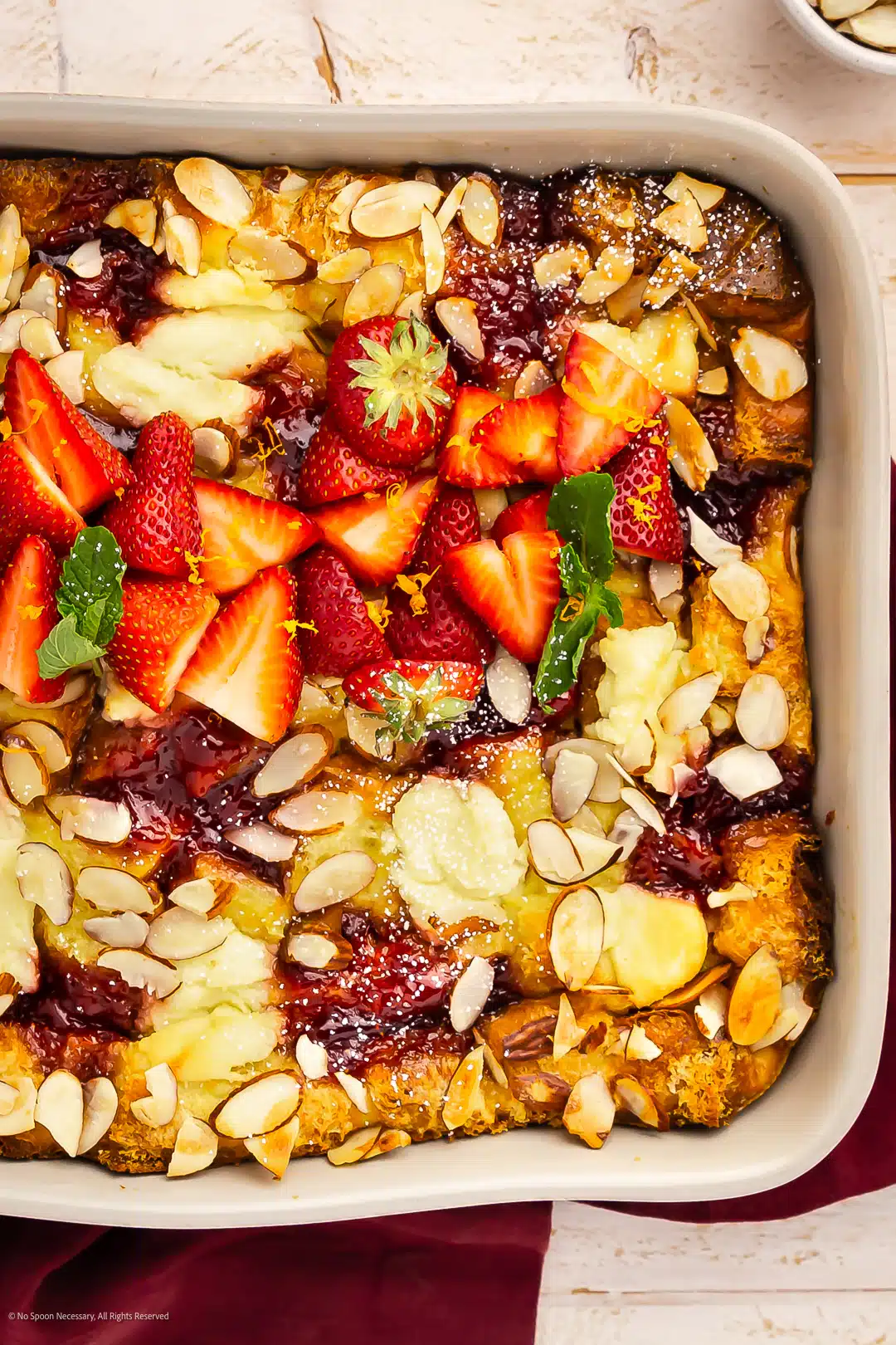 Overhead photo of a breakfast sweet casserole garnished with sliced berries and toasted almonds.
