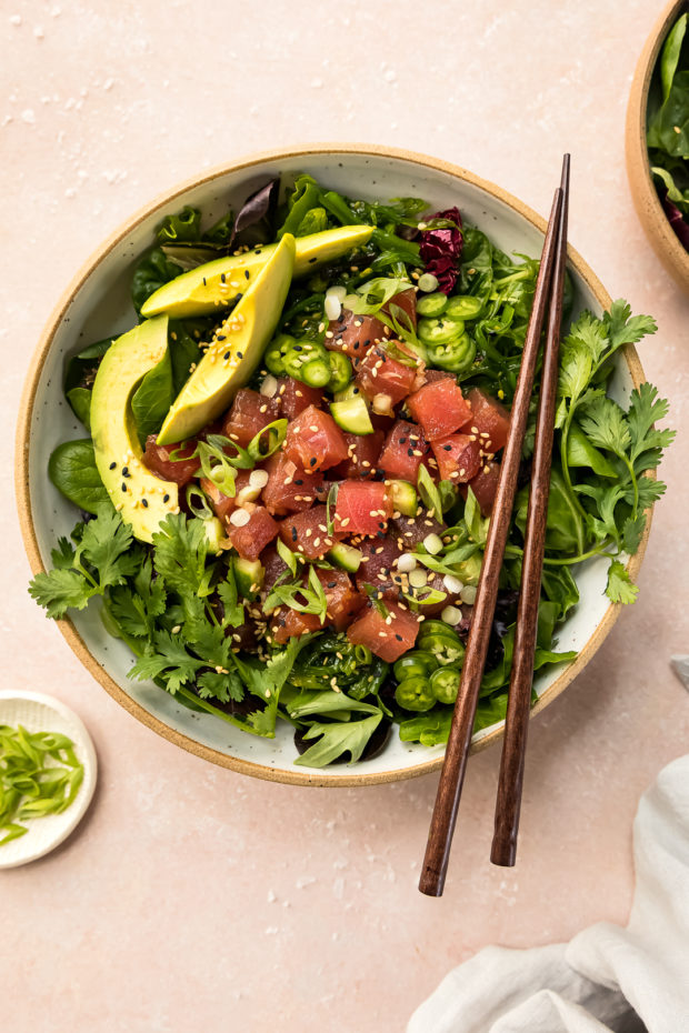 Overhead photo of a tuna poke recipe with avocado in a white bowl with wood chopsticks. 