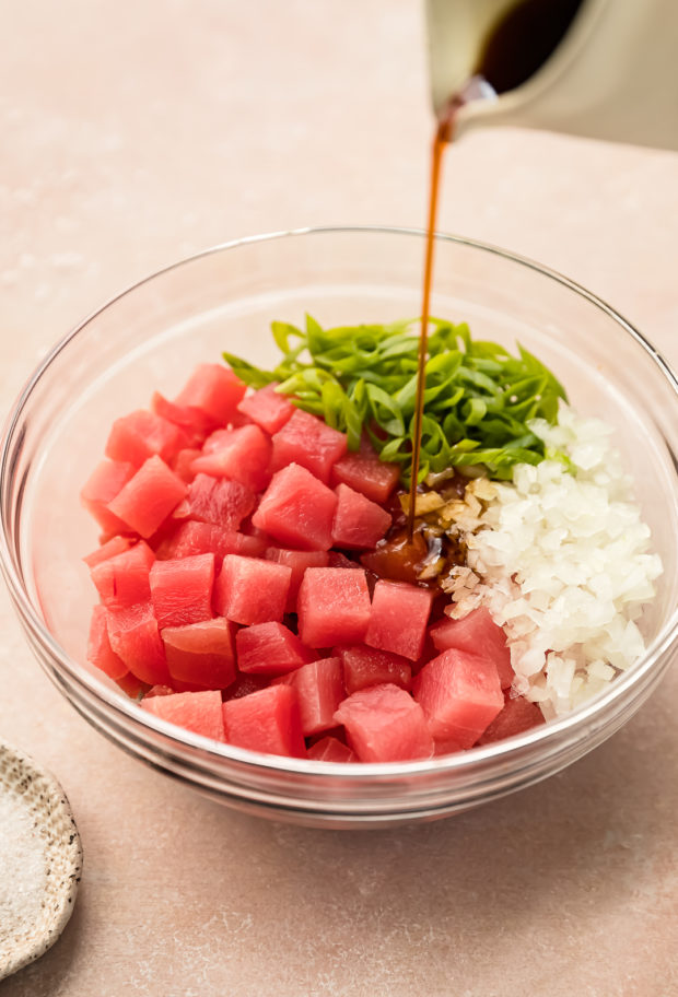 Angled photo of poke dressing being pored over poke salad ingredients in a large mixing bowl.