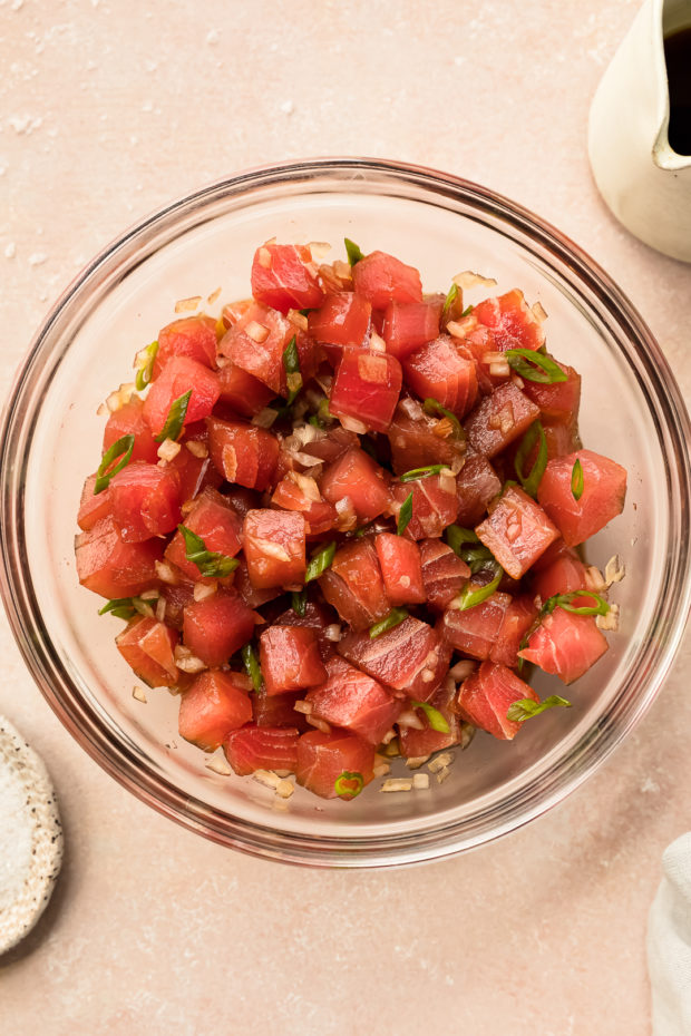 Overhead photo of cubed tuna with poke dressing in a glass mixing bowl.