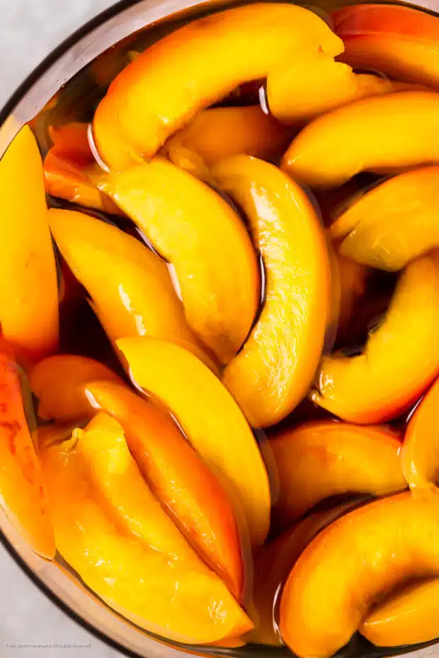 Close-up photo of thick slices of fresh peaches soaking in almond syrup.