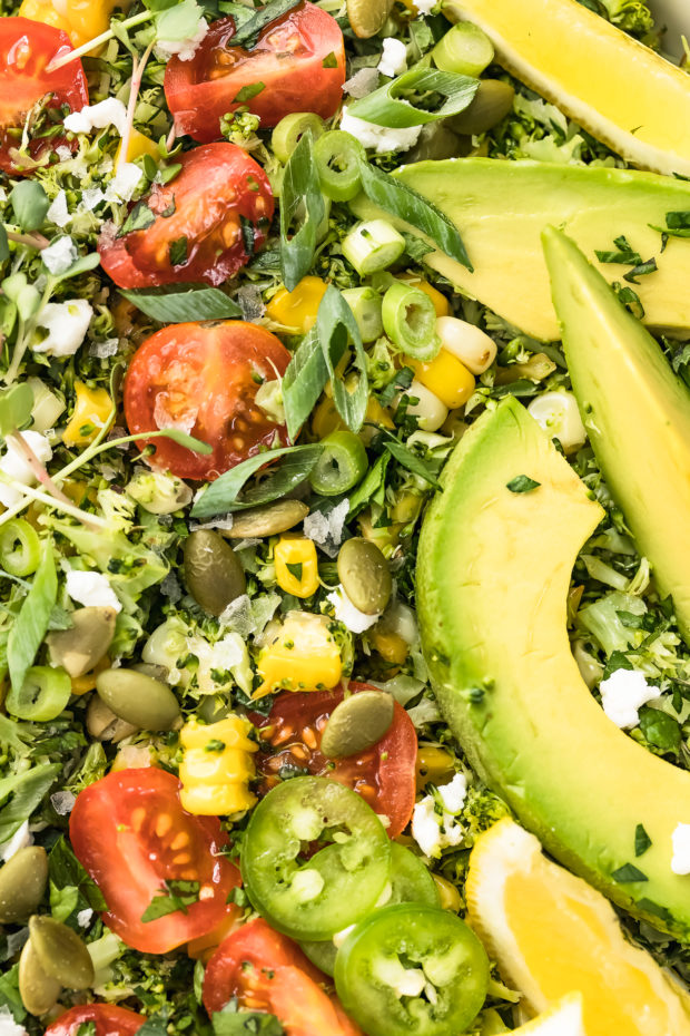 Overhead, up-close shot of Summer Corn & Broccoli Tabbouleh salad and garnished with microgreens, sliced scallions ,avocados and lemon wedges.