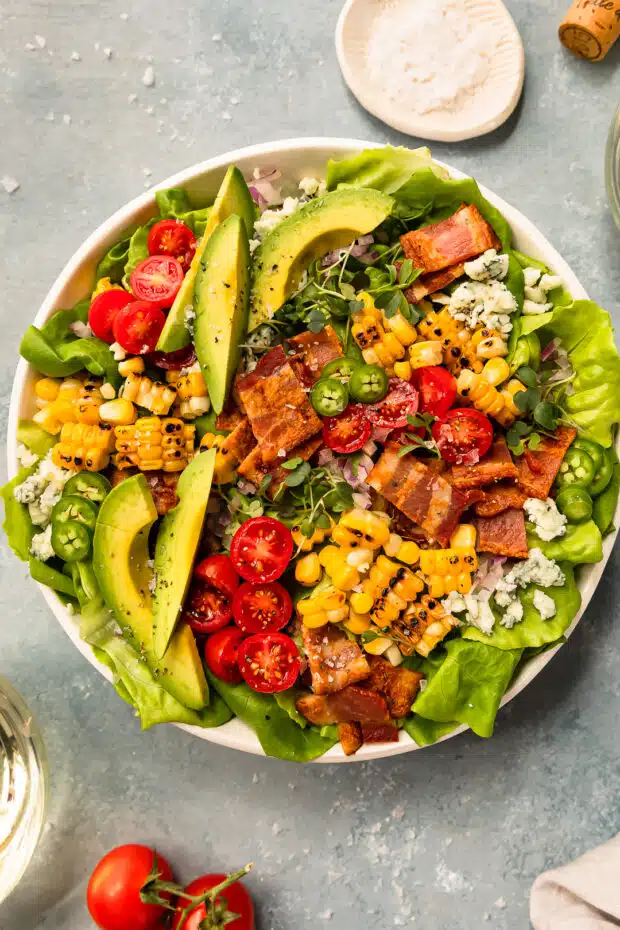 Overhead photo of a blt salad with avocado and corn in a white bowl.