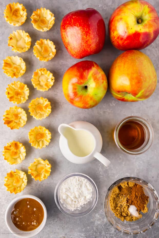 Overhead photo of puff pastry cups, apples, cream, maple syrup, and sugar neatly organized on a kitchen counter.