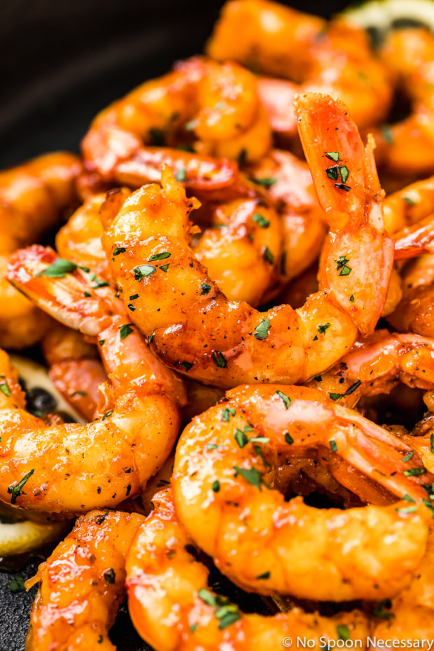 Angled, up close shot of Easy Cajun Honey Butter Shrimp in a cast iron skillet garnished with minced parsley. 