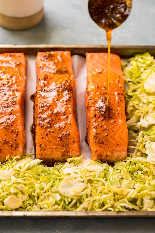 Action photo of honey dijon sauce being drizzled over salmon and sprouts.