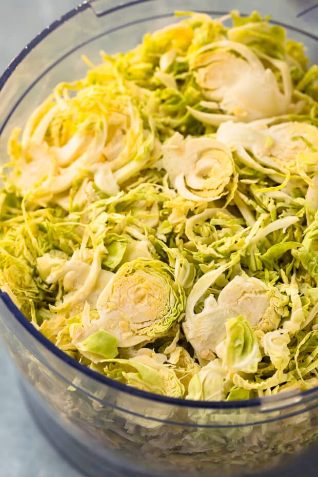 Close-up photo of sliced brussel sprouts in a food processor bowl.
