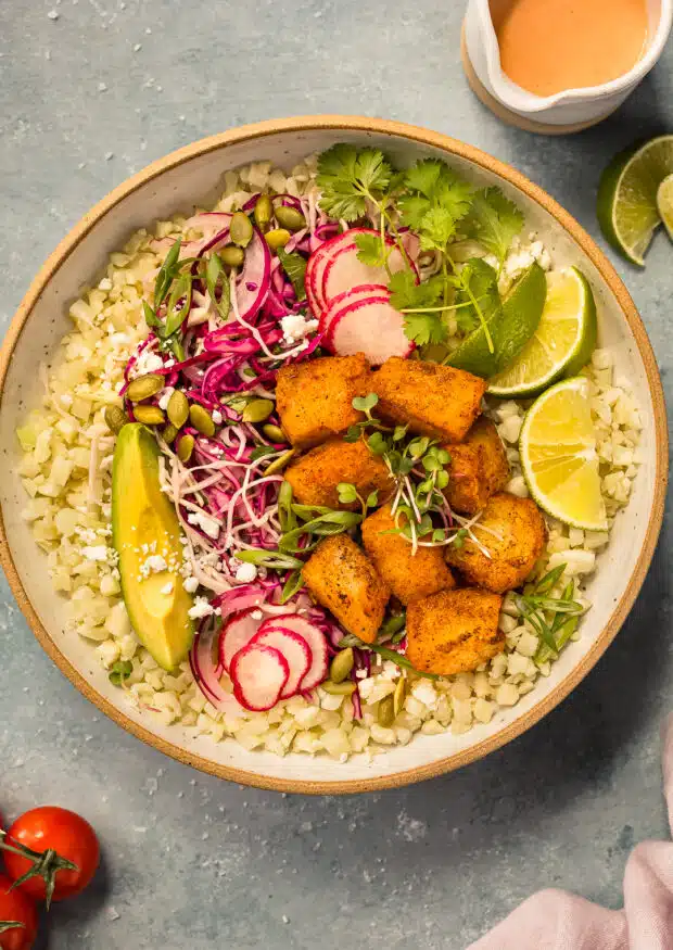 Overhead photo of a fish bowl with crispy pieces of fish, taco slaw, avocado, and cauliflower rice.