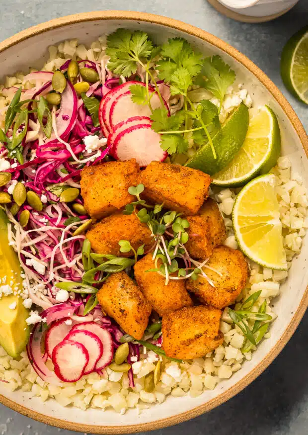 Close-up photo of a taco bowl with crispy white fish, slaw, rice, and veggies.