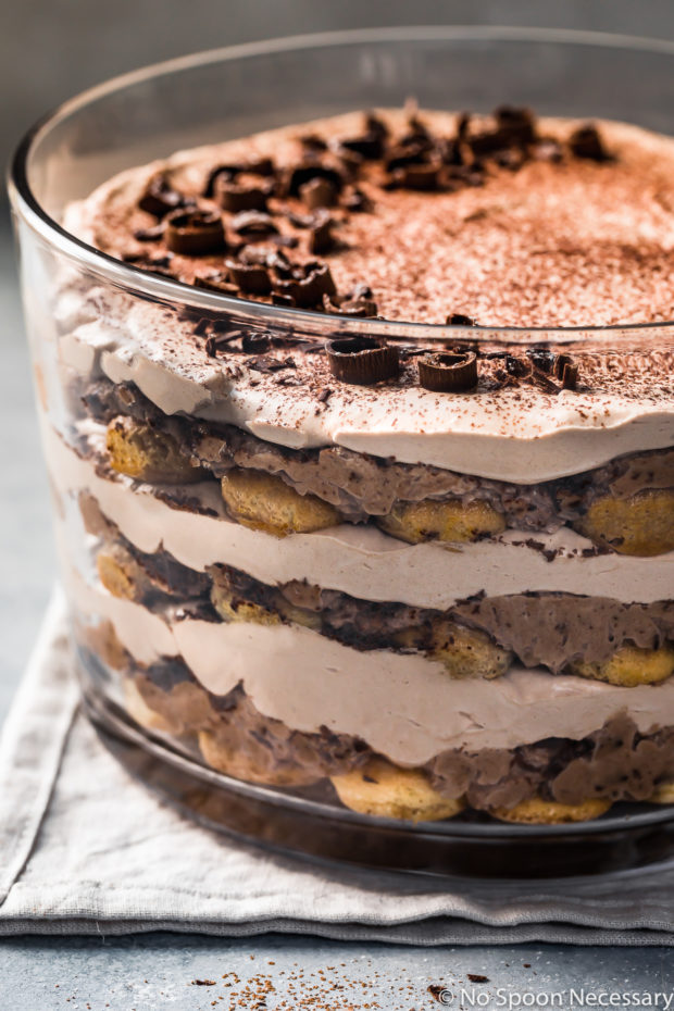 Slightly angled, straight on up close shot of an Easy Chocolate Tiramisu Trifle on a pale blue linen with cocoa powder dusted around the trifle bowl.