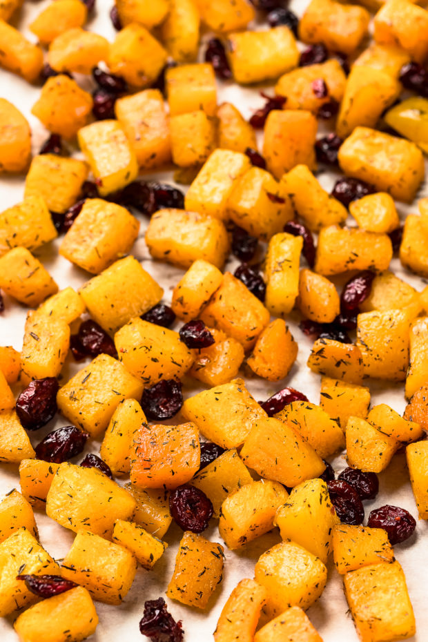 Angled shot of diced maple roasted butternut squash and dried cranberries on a parchment paper lined sheet pan - photo of step 2 of the Butternut Squash Salad recipe.