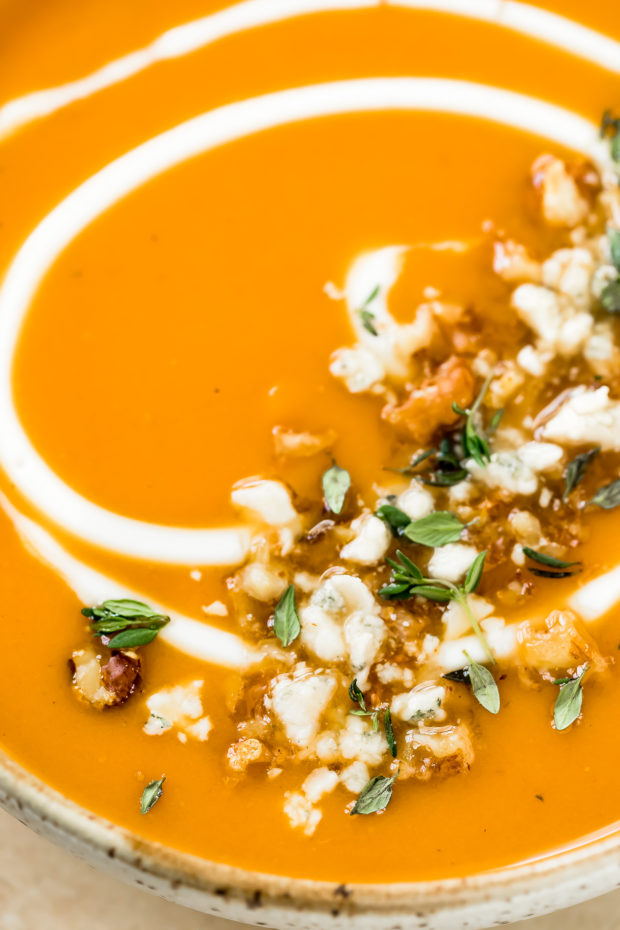 Slightly angled, extreme close-up photo of easy Sweet Potato Soup garnished with walnuts, thyme and gorgonzola. 