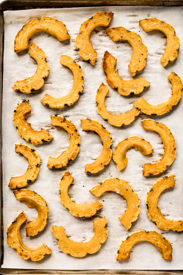 Overhead photo of roasted delicata squash rounds on a parchment paper lined sheet pan - photo of step 3 of the recipe.