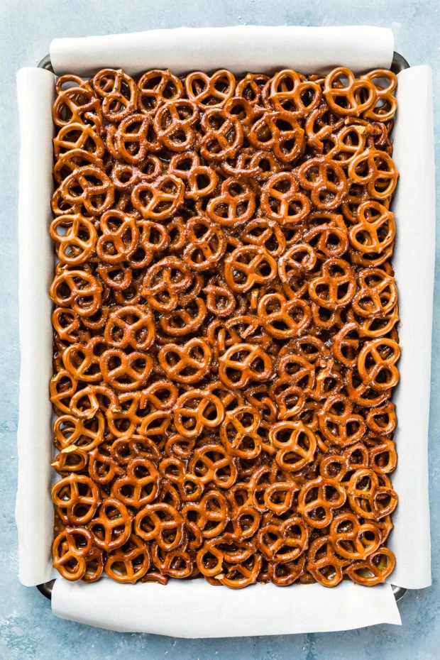 Overhead photo of a rimmed cookie sheet lined with parchment paper and filled with a layer of pretzels covered with toffee - photo of step 5 of the recipe.