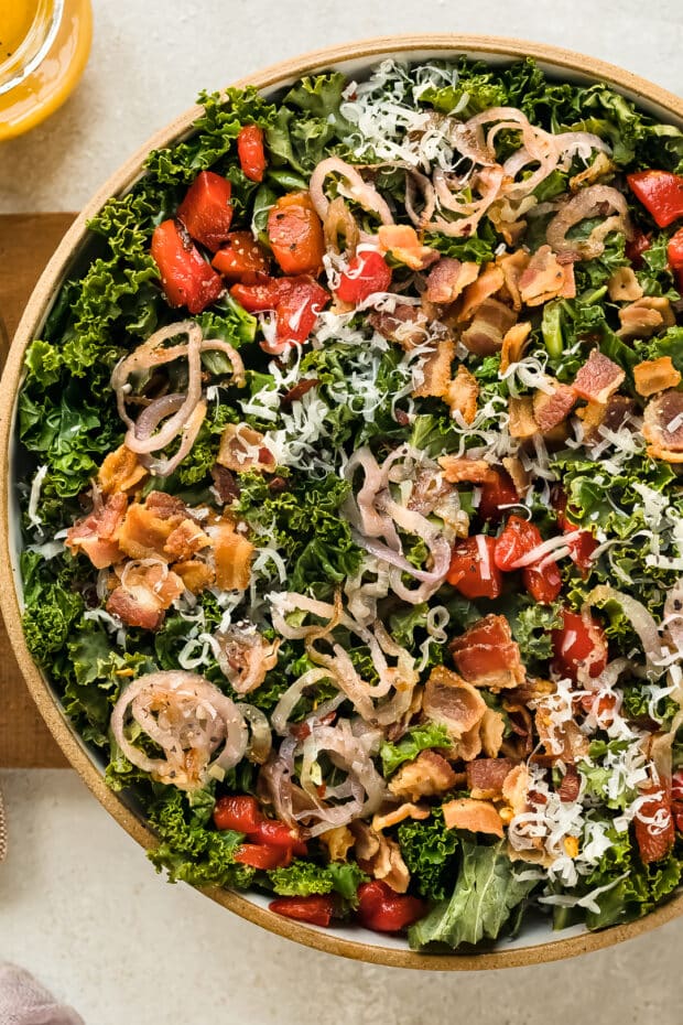 Overhead photo of kale salad warm with roasted red peppers, crispy bacon and fried shallots.