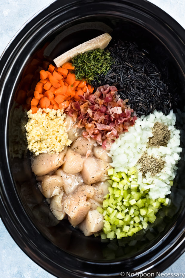 Overhead photo of all the dry ingredients needed to make Creamy Chicken and Wild Rice Soup neatly arranged in the bowl of a black slow cooker - photo of step 2 of the Slow Cooker Creamy Chicken and Wild Rice Soup recipe.