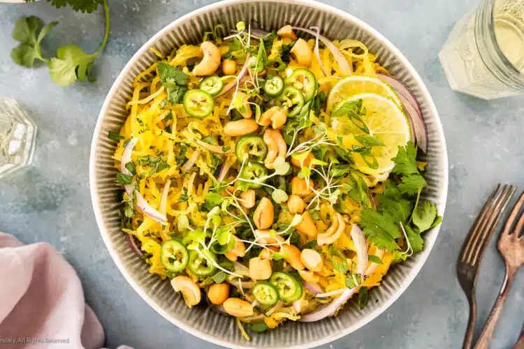 Overhead photo of spaghetti squash salad with herbs and nuts in a white serving bowl.